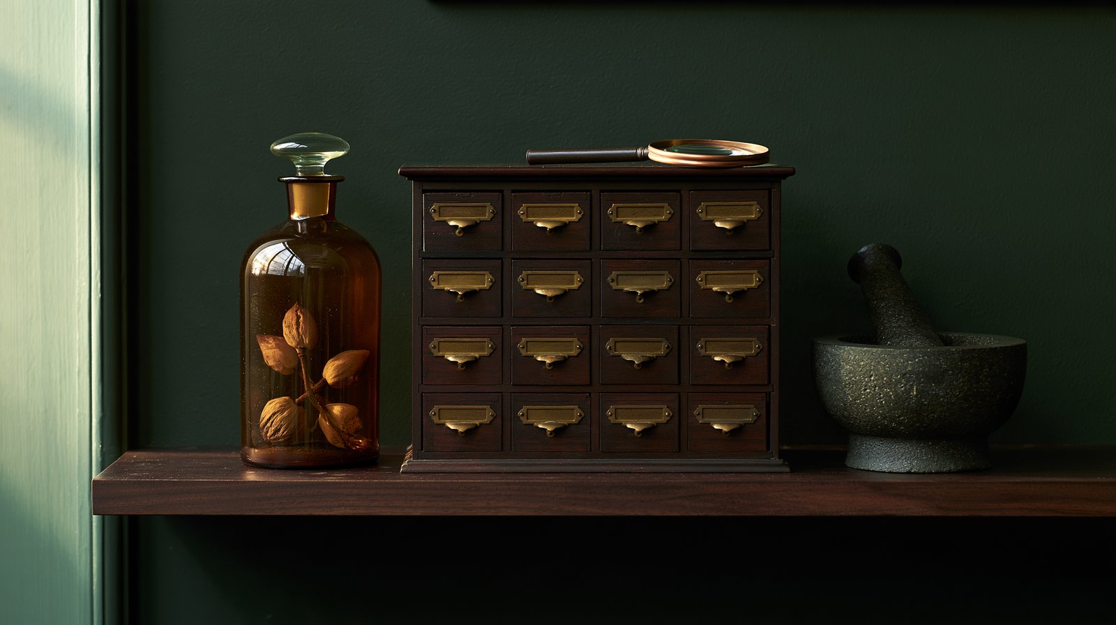 Dark walnut wall shelf with a small sixteen-drawer cabinet, an amber glass bottle, a granite mortar and a copper magnifying glass